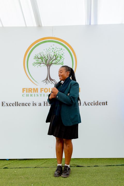 A learner presenting on stage in front of the school crest