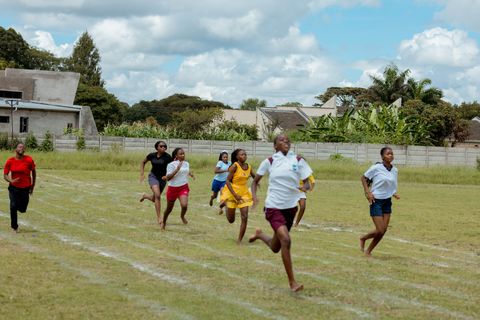 Learners racing on the school sports field with campus buildings behind them
